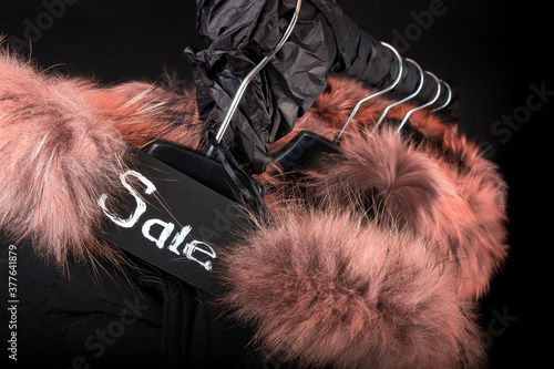 Sale sign. A lot of black coats, jacket with fur on hood hanging on clothes rack.