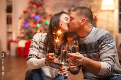 Happy girlfriend kissing his boyfriend while holding a hand fireworks on christmas day.