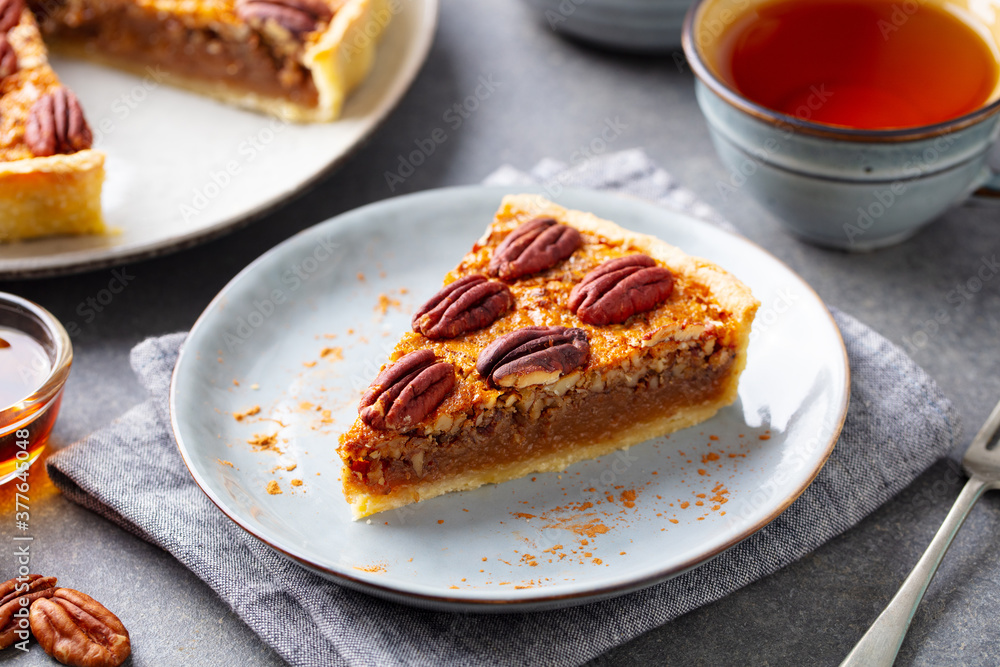 Pecan pie, tart piece on a plate with cup of tea. Grey background. Close up. Pecan pie, tart piece on a plate with cup of tea. Grey background. Close up.