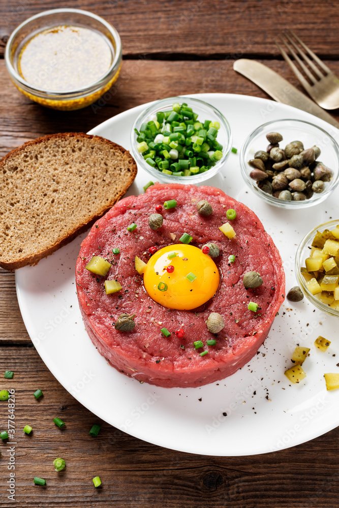 Beef tartare with capers , fresh onion and pickled cucumber on white plate on wooden background. Beef tartare with capers , fresh onion and pickled cucumber on white plate on wooden background.