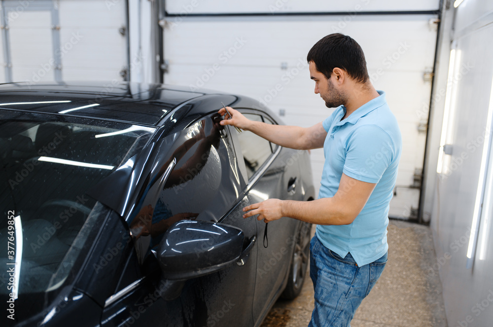 Male worker tries on wetted car tinting, tuning Male worker tries on wetted car tinting, tuning