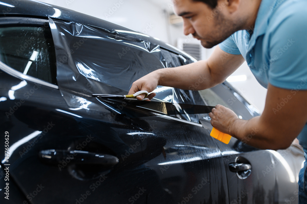 Worker holds film, car tinting installation