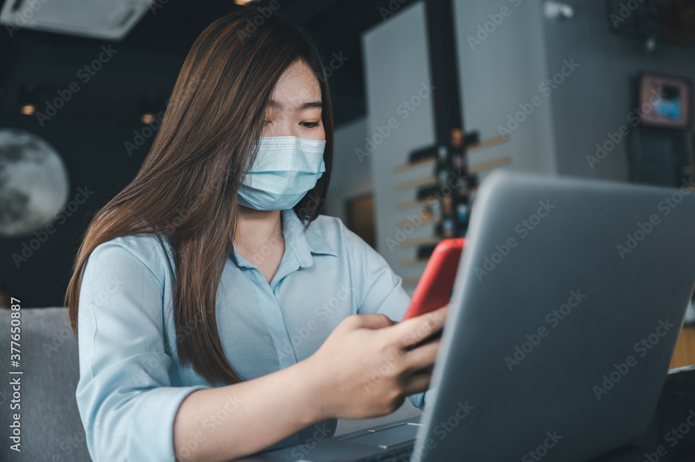 Asian woman wearing a mask uses a smartphone in a coffee shop. Asian woman wearing a mask uses a smartphone in a coffee shop.