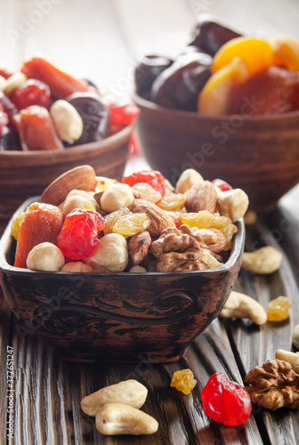 Assorted nuts and dried fruits in clay bowl on wooden kitchen table closeup