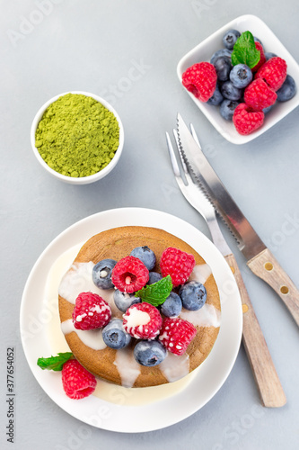 Stack of matcha pancakes served with condensed milk, blueberry and raspberry on white plate, vertical, top view