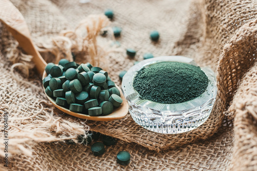 Fototapeta Naklejka Na Ścianę i Meble -  Spirulina chlorella tablets on a spoon, powder in a glass bowl. Super food for a healthy diet, vitamins, minerals, trace elements for health and beauty