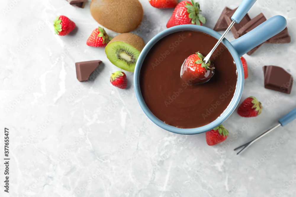 Dipping strawberry into fondue pot with chocolate on light grey marble table, top view. Space for text Dipping strawberry into fondue pot with chocolate on light grey marble table, top view. Space for text