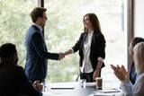 Young businessman handshake happy female colleague or employee congratulate with job success. Smiling diverse businesspeople shake hands get acquainted greeting at office meeting. Cooperation concept.