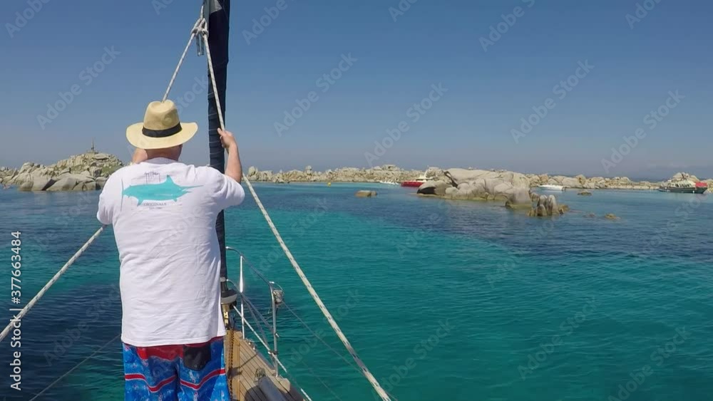 Caucasian man leans on ropes over front of sailboat on turquoise sea Caucasian man leans on ropes over front of sailboat on turquoise sea
