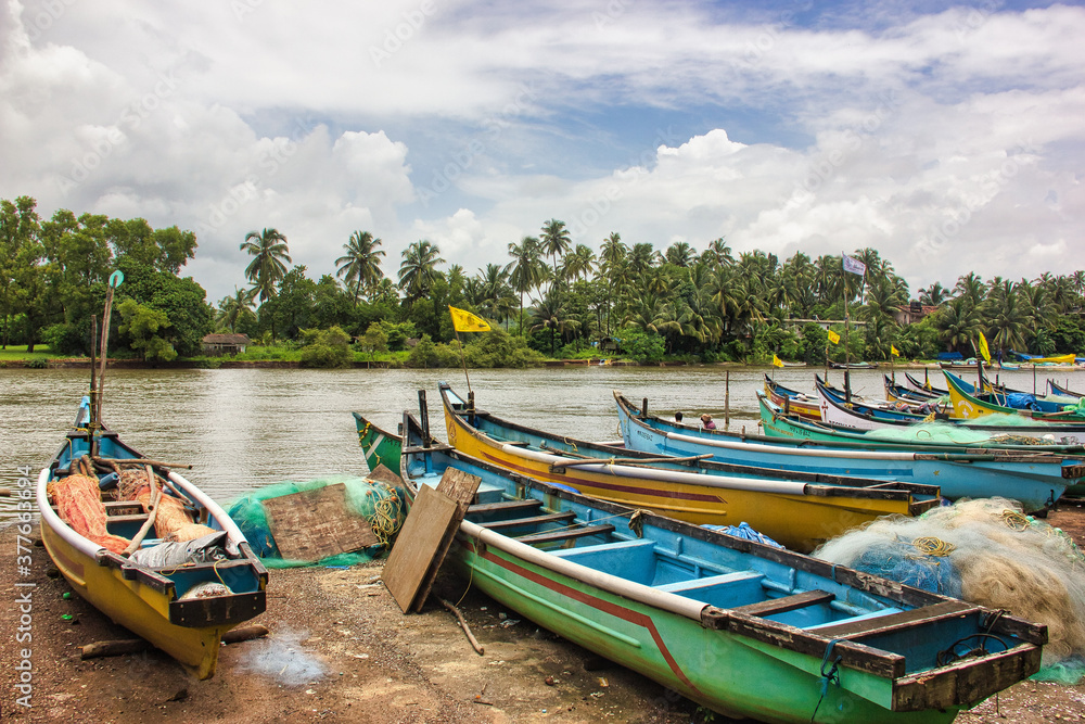 Boats in river in Goa with blue dramatic sky and green trees, India