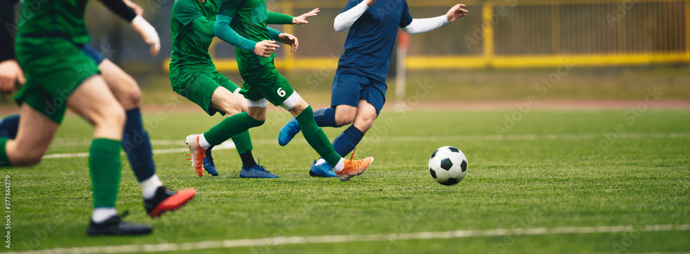 Teenagers in soccer duel. Boys in two football teams running after classic soccer ball. Horizntal sports background. Legs of young players on football pitch Teenagers in soccer duel. Boys in two football teams running after classic soccer ball. Horizntal sports background. Legs of young players on football pitch