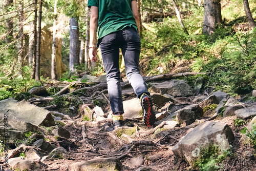 Man climbs mountain steam river. Sporty clothes and backpack. Hiking boots in outdoor action. Top View of Boot on the trail. Close-up Legs In sport trekking shoes on rocky stones of Mountain river