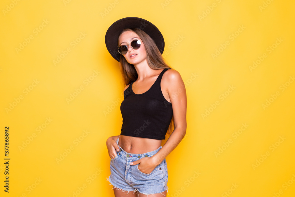 Cheerful trending young woman in hat and sunglasses on yellow background Cheerful trending young woman in hat and sunglasses on yellow background