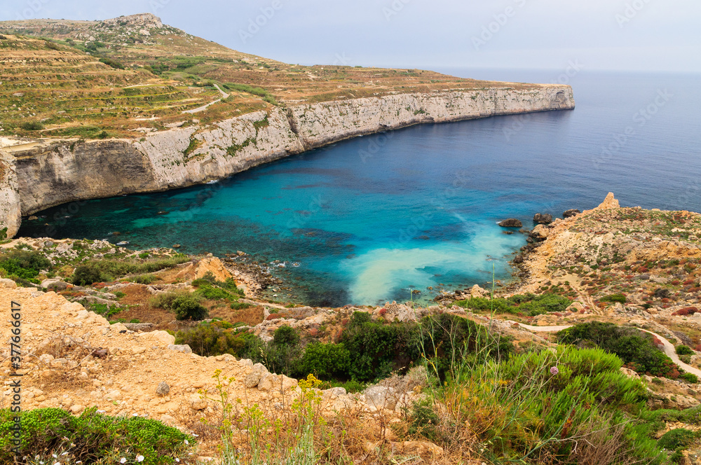 Incredible colors of view on colorful rocks on coastline in Malta. Juicy blue and green sea, blue sky. Beautiful landscapce. Hiking way on cliffs. Unforgettable scenery.