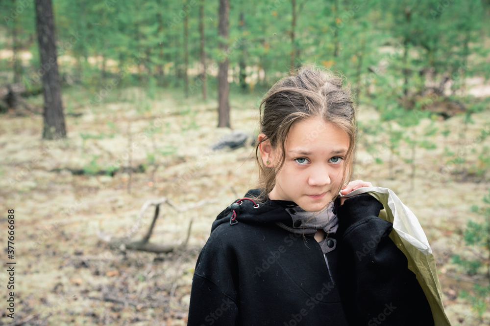 Tortured look of girl in jacket standing in the forest with package behind her back after picking mushrooms. Tortured look of girl in jacket standing in the forest with package behind her back after picking mushrooms.