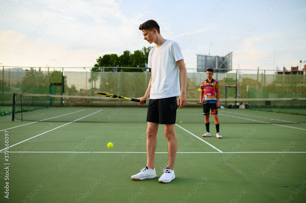 Male tennis players with rackets hits the balls