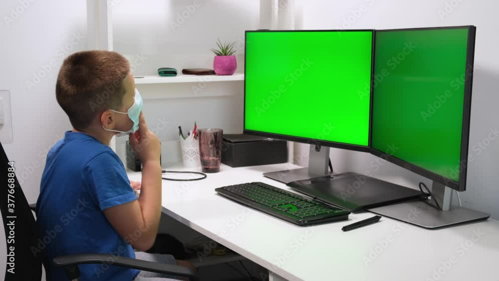 Child boy studying homework against two green monitors or screens during online lesson at home. E-learning, webinar. Online distance education for children caused by coronavirus pandemia quarantine Child boy studying homework against two green monitors or screens during online lesson at home. E-learning, webinar. Online distance education for children caused by coronavirus pandemia quarantine