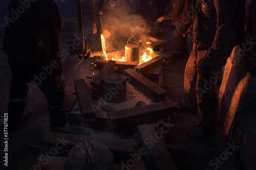The workers are pouring molten metal to molds for casting. Casting is a manufacturing process in which a liquid material is usually poured into a mold.