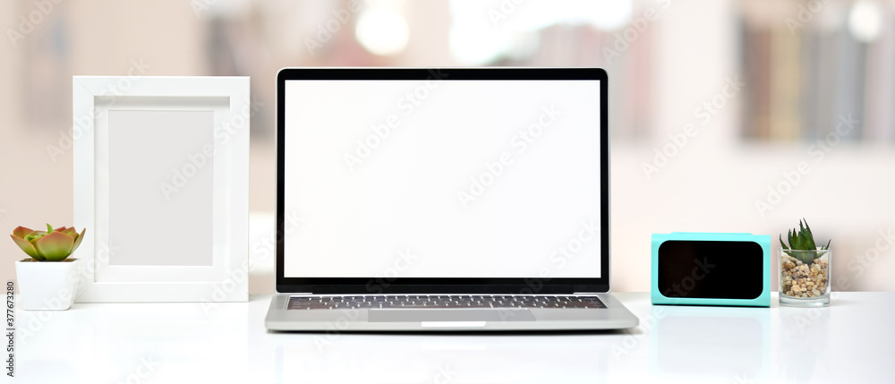 Workspace mock up with blank screen laptop, clock digital, frame and cactus on white background in office. Front view. Workspace mock up with blank screen laptop, clock digital, frame and cactus on white background in office. Front view.