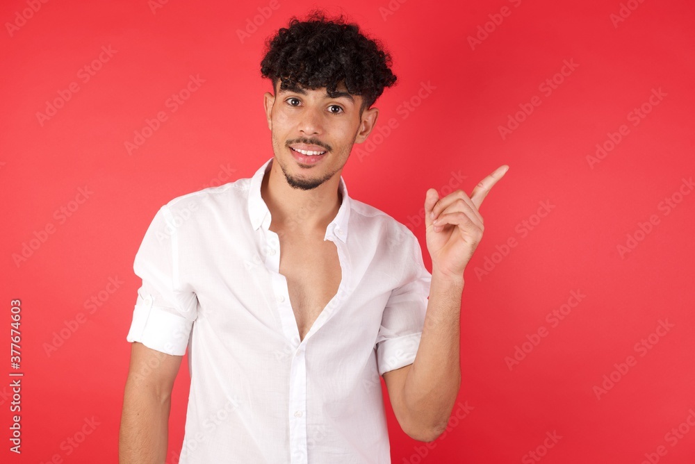 Young arab man with afro hair wearing shirt standing over isolated red background holding finger up having idea and posing Young arab man with afro hair wearing shirt standing over isolated red background holding finger up having idea and posing