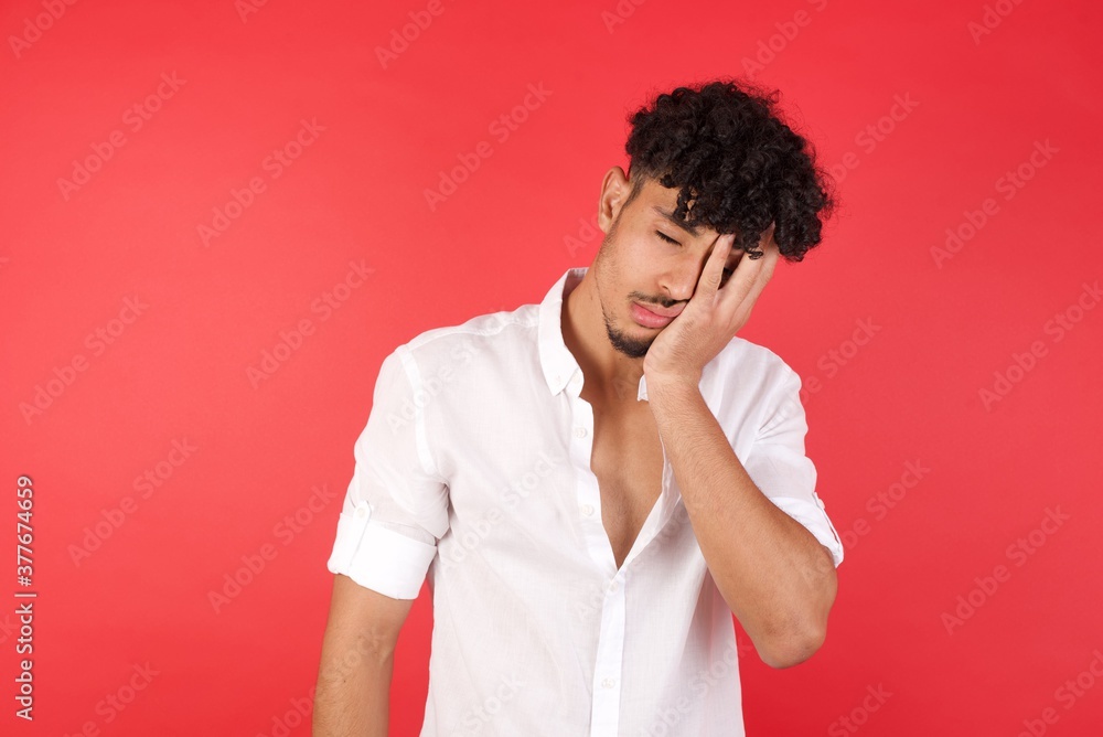 Tired overworked Young arab man with afro hair wearing shirt standing has sleepy expression, gloomy look, covers face with hand, has eyes shut, gasps from tiredness, fatigue after party Tired overworked Young arab man with afro hair wearing shirt standing has sleepy expression, gloomy look, covers face with hand, has eyes shut, gasps from tiredness, fatigue after party