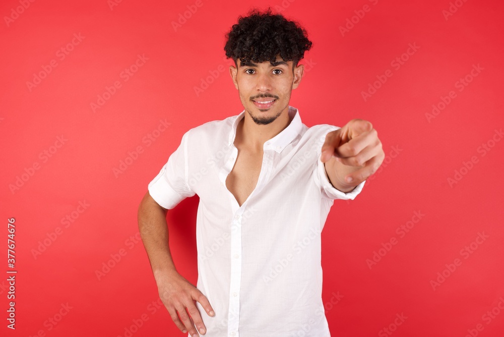 Young arab man with afro hair wearing shirt standing over isolated red background pointing at camera with a satisfied, confident, friendly smile, choosing you Young arab man with afro hair wearing shirt standing over isolated red background pointing at camera with a satisfied, confident, friendly smile, choosing you