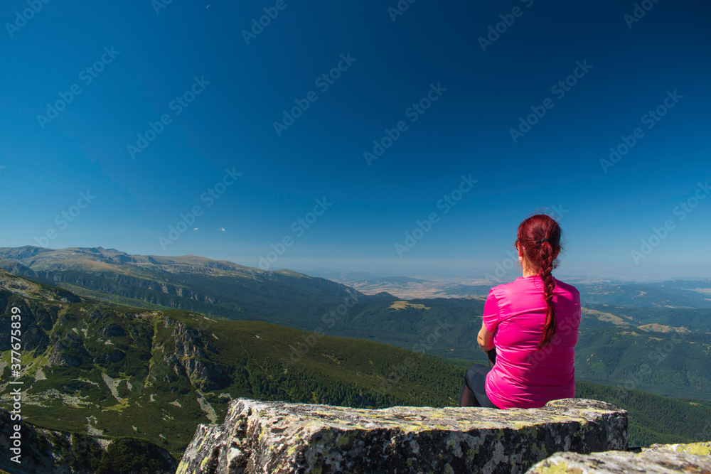Young lady enjoying the scenery on the top of a mountain peak.