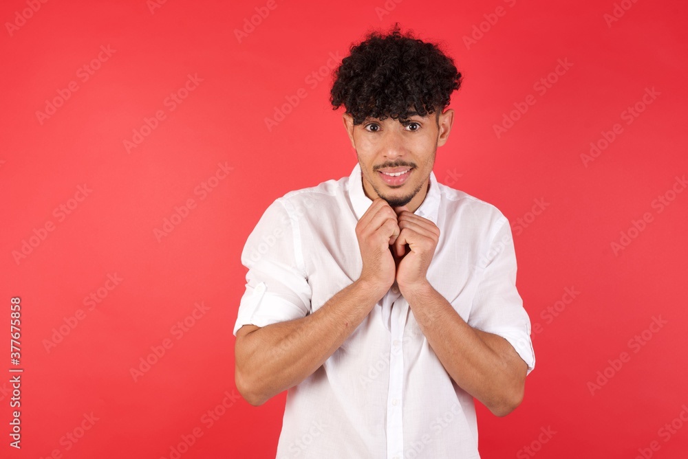 Positive Young arab man with afro hair wearing shirt standing smiles happily, glad to receive pleasant news from interlocutor, keeps hands together. People, and emotions concept. Positive Young arab man with afro hair wearing shirt standing smiles happily, glad to receive pleasant news from interlocutor, keeps hands together. People, and emotions concept.