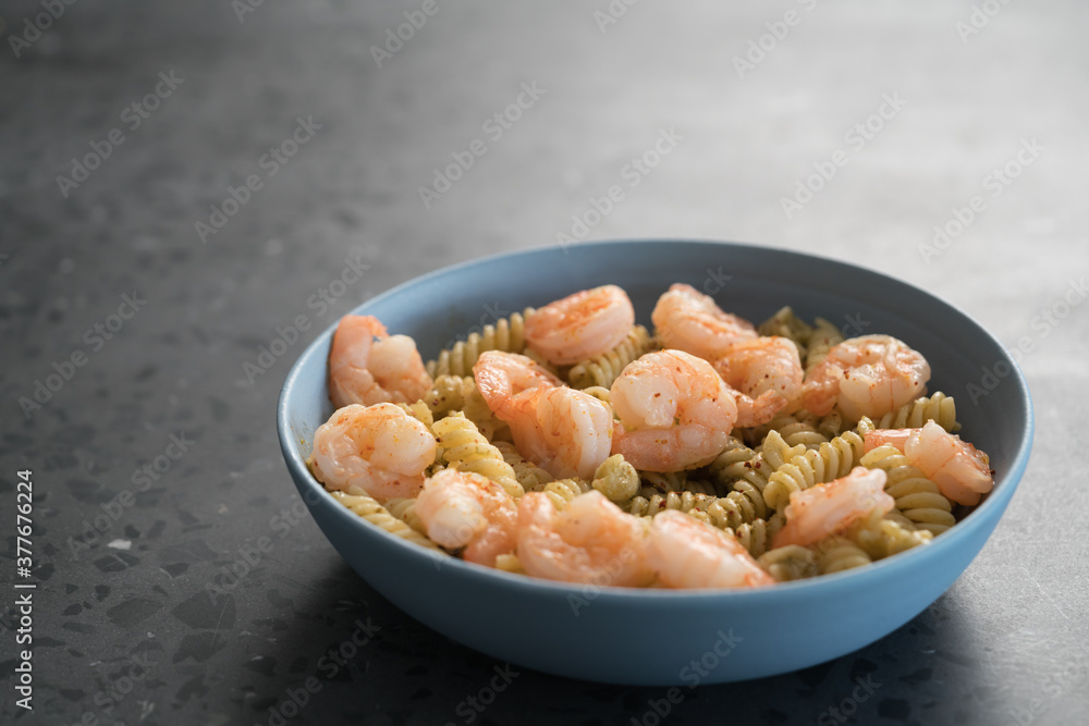 Fusilli with shrimps and pesto in a blue bowl on concrete background Fusilli with shrimps and pesto in a blue bowl on concrete background
