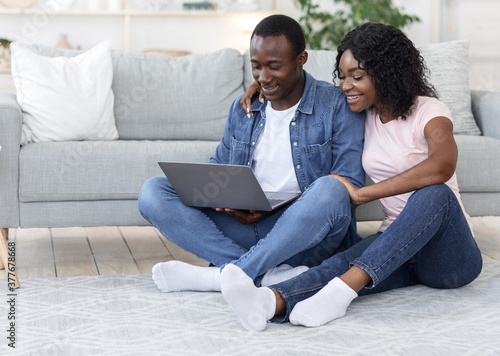 African american lovers sittng on floor at home, using laptop