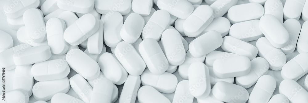Medical background of many white capsule tablets or pills on the table. Full frame background. Healthcare pharmacy and medicine concept banner. Painkillers or prescription drugs consumption Medical background of many white capsule tablets or pills on the table. Full frame background. Healthcare pharmacy and medicine concept banner. Painkillers or prescription drugs consumption