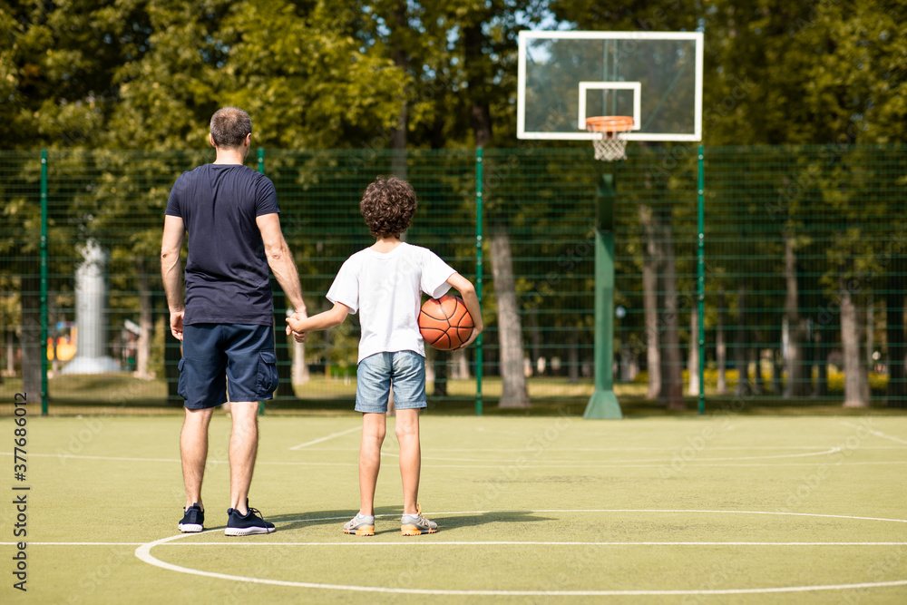 Obraz premium Man posing with son on basketball pitch back view