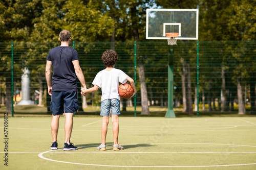 Man posing with son on basketball pitch back view