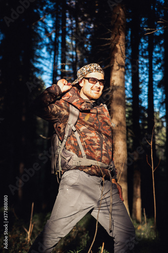 Hiker hiking in autumn forest. Male hiker in camouflage jacket with backpack looking to the side walking in forest. Caucasian handsome male outdoors in nature. Concept of forest wear, navigation.
