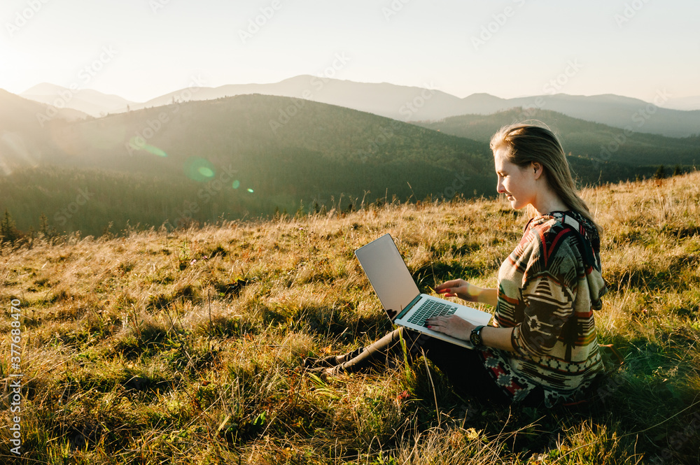 Woman traveler using laptop computer while enjoying sunset in mountains. Freelancer girl working on netbook during vacation holidays in autumn. Distant work and travel, freelance as lifestyle concept. Woman traveler using laptop computer while enjoying sunset in mountains. Freelancer girl working on netbook during vacation holidays in autumn. Distant work and travel, freelance as lifestyle concept.