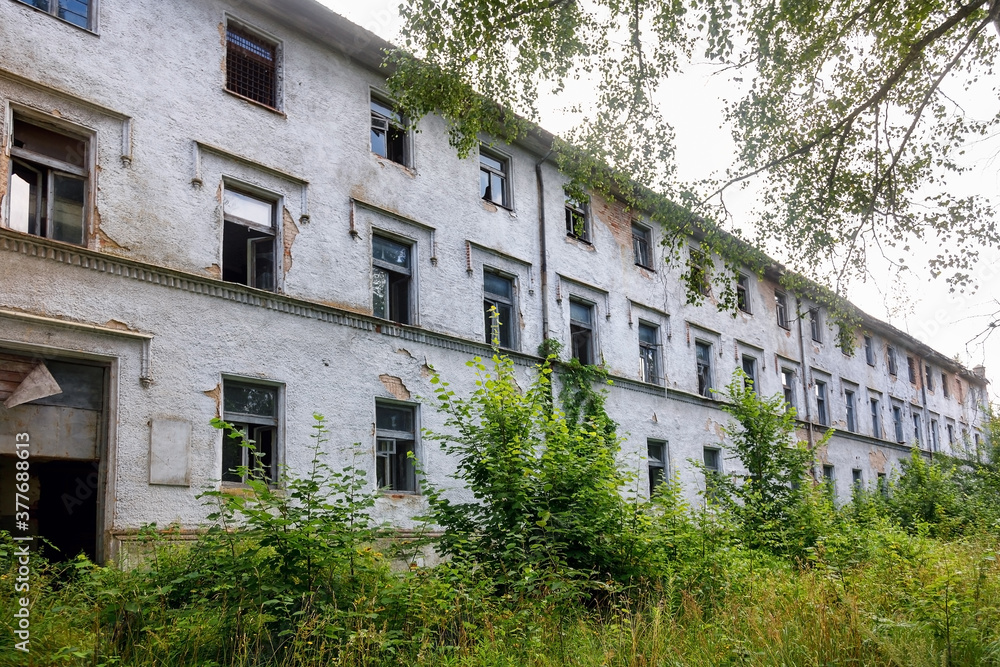 An old abandoned hospital building overgrown with grass and greenery