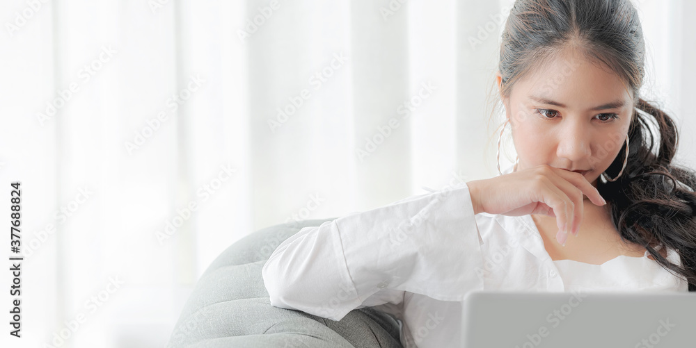 Portrait of young beautiful asian woman using latop, looking and thinking while sitting on sofa in living room at home. Portrait of young beautiful asian woman using latop, looking and thinking while sitting on sofa in living room at home.