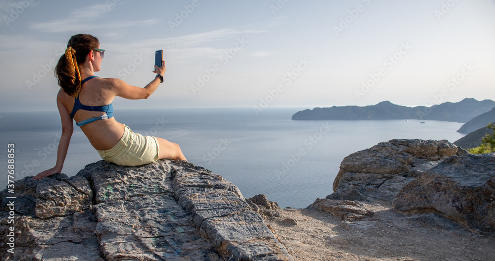 A woman taking pictures with her phone of the sea view over a mountain A woman taking pictures with her phone of the sea view over a mountain