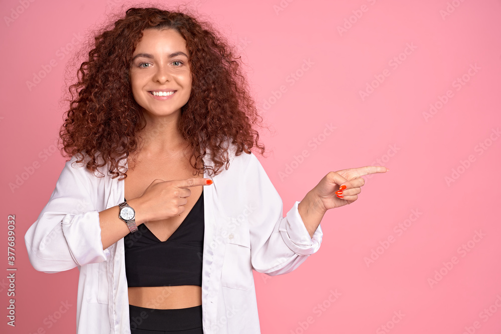 Shall we go already. Portrait of charming european redhead female in trendy outfit gazing straight and pointing right with index finger as if asking question or suggesting new direction to take walk Shall we go already. Portrait of charming european redhead female in trendy outfit gazing straight and pointing right with index finger as if asking question or suggesting new direction to take walk