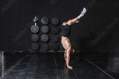 Tableau sur toile Young strong fit muscular man doing hand stand and walk in the gym as hardcore c