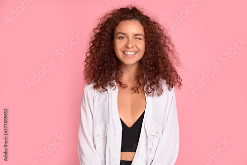 Photo of pretty cheerful girl with red curly hair smiling looking at camera over pink background.