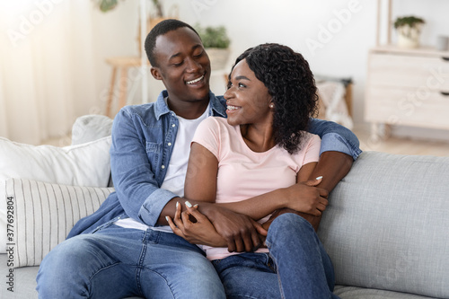 Happy african couple cuddling on sofa at home