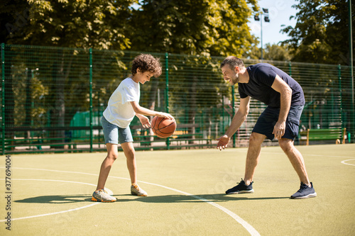 Sportive man teaching boy how to play basketball