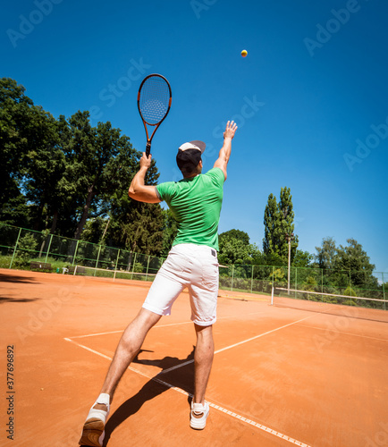 Young athletic man playing tennis on the court.