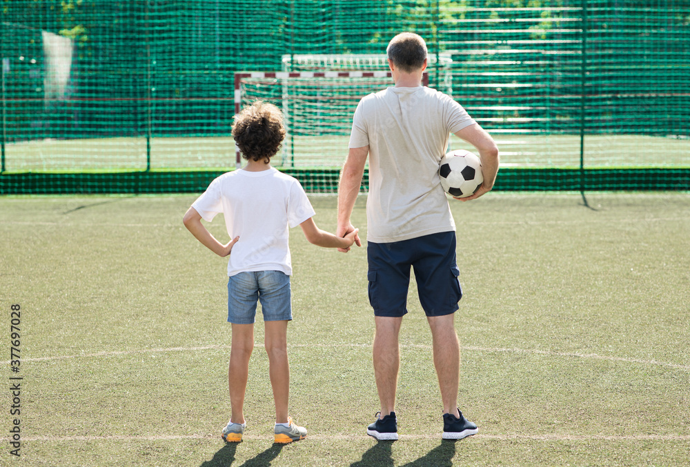 Dad posing with little boy on football pitch, back view