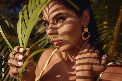 Portrait of a beautiful brunette woman in bikini with palm leaf shadows on her face. Summer happy vacation on the sea beach