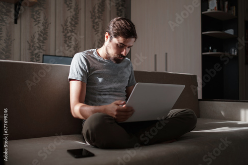 Remote Job. Man Working On Laptop Sitting On Sofa At Home.