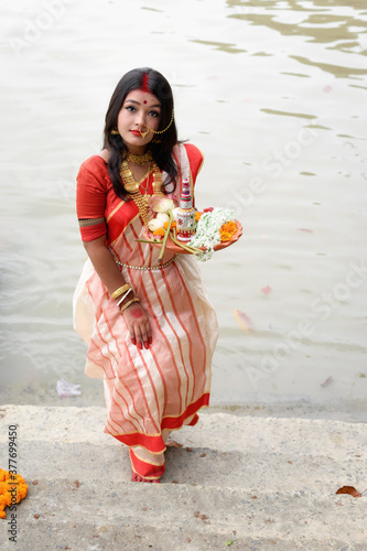 Portrait of beautiful Indian girl wearing traditional Indian saree, gold jewellery and bangles holding plate of religious offering. Maa Durga agomoni shoot concept photo