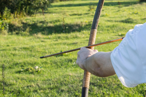 Strong male hands hold an arrow and a bow for shooting. Outdoor activities with archery