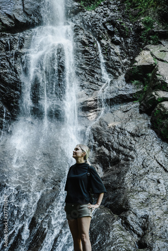 Fototapeta Naklejka Na Ścianę i Meble -  young woman on the background of a mountain waterfall with a ponytail 